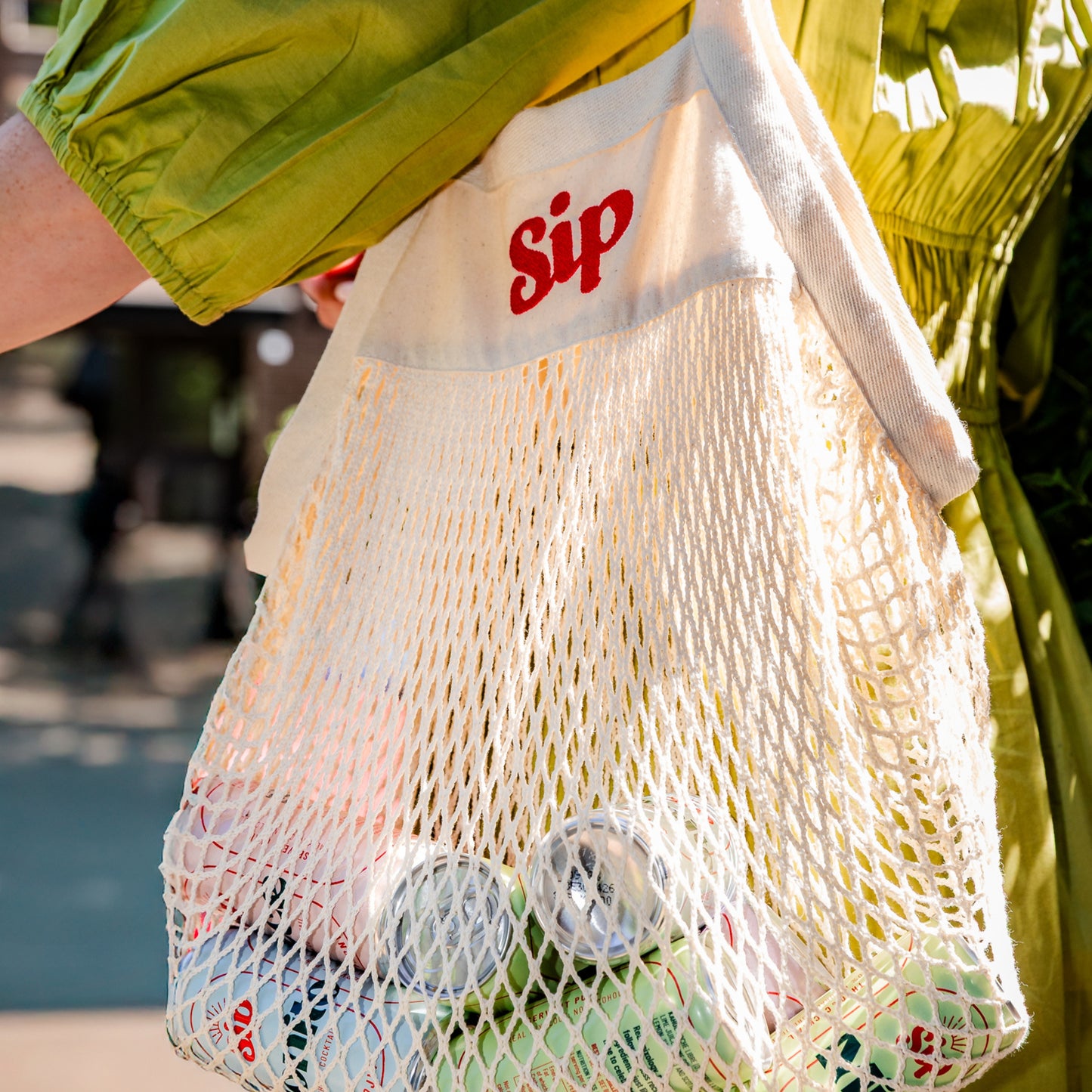 Sip mesh tote bag carried on the shoulder, filled with cans of Sip alcohol-free cocktails
